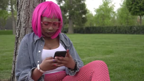 Joven mujer africana negra con cabello rosa utiliza Internet con un teléfono inteligente — Vídeos de Stock