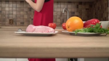 Kırmızı elbiseli genç seksi kadın mutfakta yemek hazırlıyor ve dans ediyor, ağır çekimde.