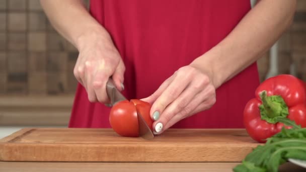 Uma mulher na cozinha corta um tomate vermelho com uma faca, câmera lenta — Vídeo de Stock