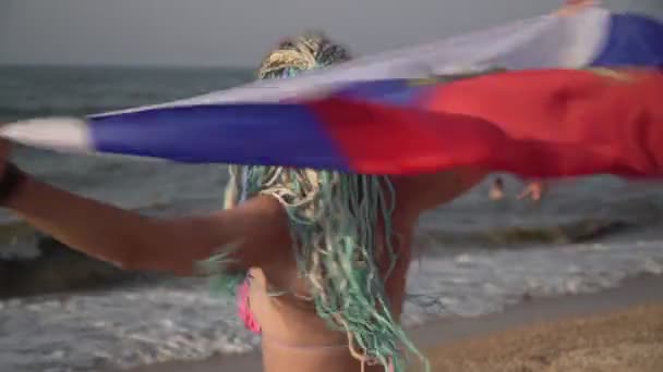 Mooie vrouw met de vlag van Rusland aan zee. Gelukkige vrouw toerist met Russische vlag op het strand — Stockvideo
