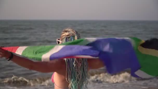 Mooie vrouw met Zuid-Afrikaanse vlag aan zee. Gelukkige vrouw toerist met Zuid-Afrikaanse vlag op het strand — Stockvideo