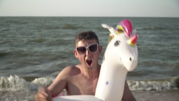 Homme drôle avec une bague en caoutchouc. L'homme joyeux danse avec un anneau gonflable en forme de licorne sur la mer — Video