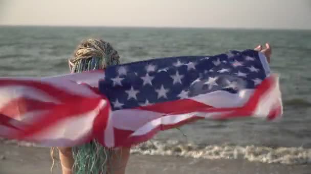 Красивая женщина с флагом США у моря. Счастливая туристка с флагом Соединенных Штатов Америки на пляже — стоковое видео