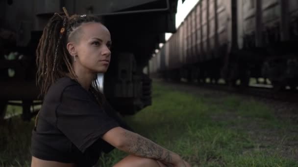 Młoda kobieta na kolei patrzy na pociąg. Portret nowoczesnej, niezależnej kobiety z dredami — Wideo stockowe