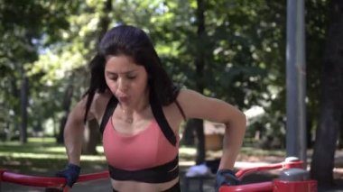 Atletik kadın açık hava barlarında şınav çekiyor.