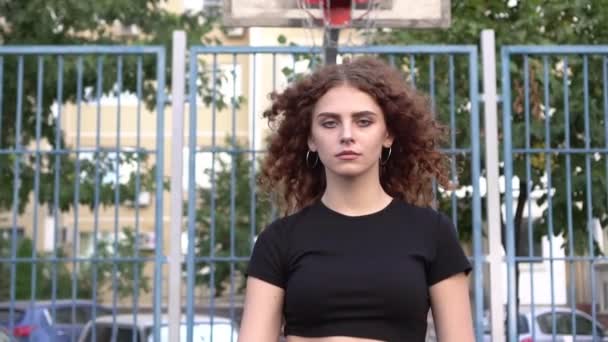 Retrato de una joven atractiva con una pelota en una cancha de baloncesto al aire libre — Vídeos de Stock