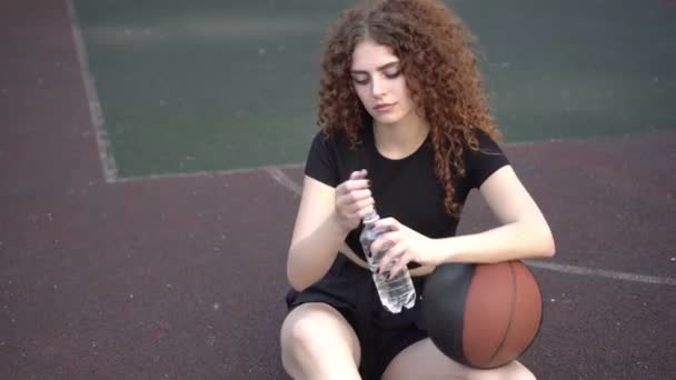 Genç ve çekici bir kadın basketbol sahasında bir şişeden su içiyor. — Stok video