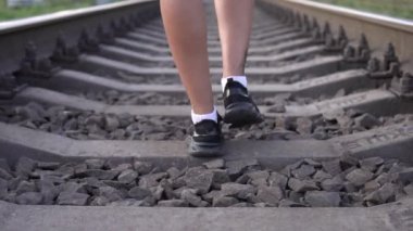 Bir kadın demiryolunda uyuyanların arasında yürüyor, bacakları yavaş çekimde.