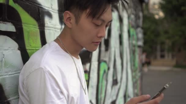 Akıllı telefonlu modern bir şehirli gencin portresi. Genç bir Koreli açık havada akıllı telefon kullanıyor. — Stok video