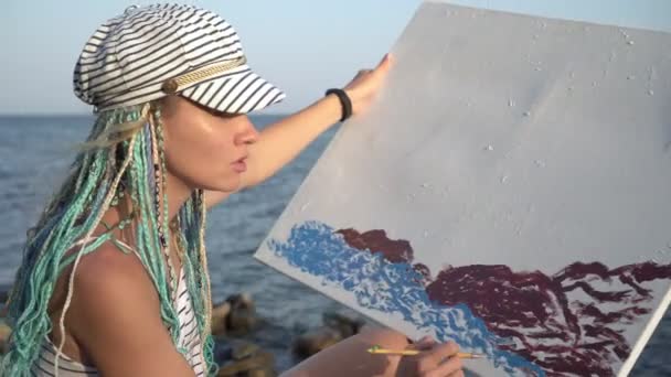 Attraente artista donna dipinge il mare su tela. Un artista contemporaneo dipinge un quadro in natura — Video Stock