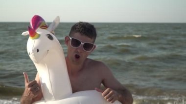 Şişme yüzüklü neşeli adam deniz sahilinde dans ediyor.