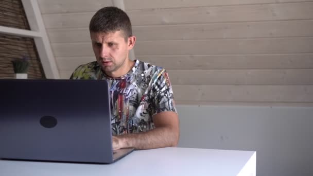 Взрослый мужчина с ноутбуком работает дома за столом. фрилансер, удаленная работа — стоковое видео
