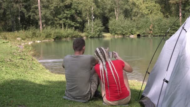 Coppia giovane uomo e donna durante un'escursione vicino alla tenda vicino al lago. Escursionismo, attività all'aperto — Video Stock