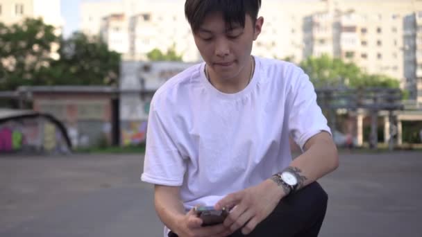 젊은 아시아인 이 야외에서 스마트폰으로 메시지를 입력 합니다. 한국의 한 십 대가 길거리에서 스마트폰을 사용하는 모습 — 비디오