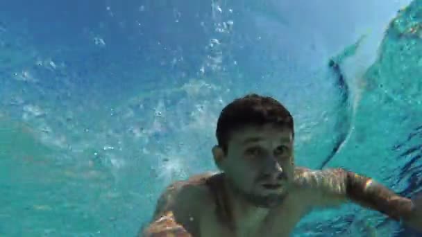 Un hombre nada en una piscina bajo el agua. Un joven hombre blanco nada bajo el agua — Vídeos de Stock