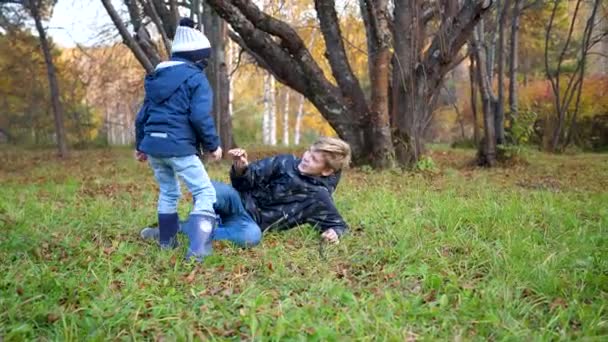 Los niños juegan en el parque, corren, caen al suelo. Risa y alegría para toda la familia. — Vídeos de Stock