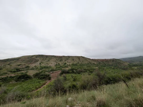 A breathtaking view of a mountain valley covered in tough grass and rocks. The light suggests changing weather, contrasting the bright sky with the deep green slopes.