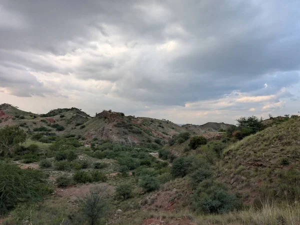Layers of hills recede to the horizon under an overcast sky. The foreground is filled with scrub, stones, and a splash of autumnal color, showcasing the wild beauty of the region.