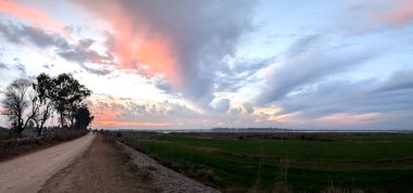 Pembe ve mor bulutlu bir nehir deltasının üzerinde panoramik günbatımı.