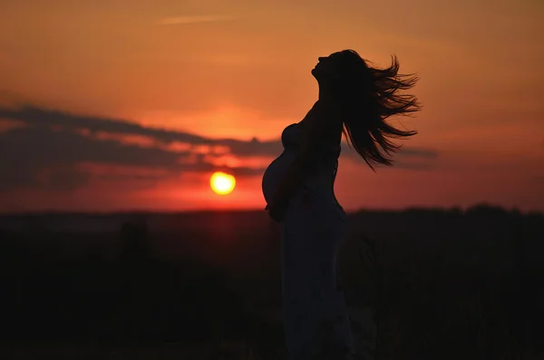 Těhotná dívka s kloboukem v oblasti pšenice na západ slunce — Stock fotografie