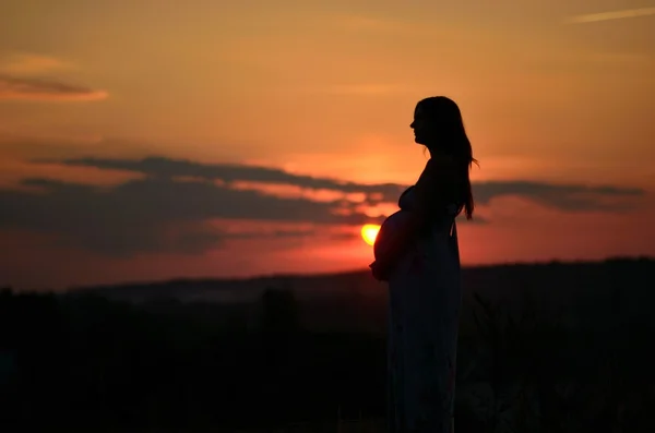 La ragazza incinta con un cappello nel campo di grano su un tramonto — Foto Stock