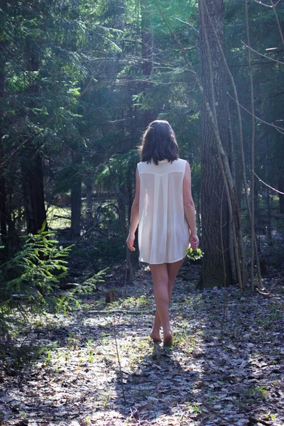 woman in a white shirt with flowers in her hand goes into the woods