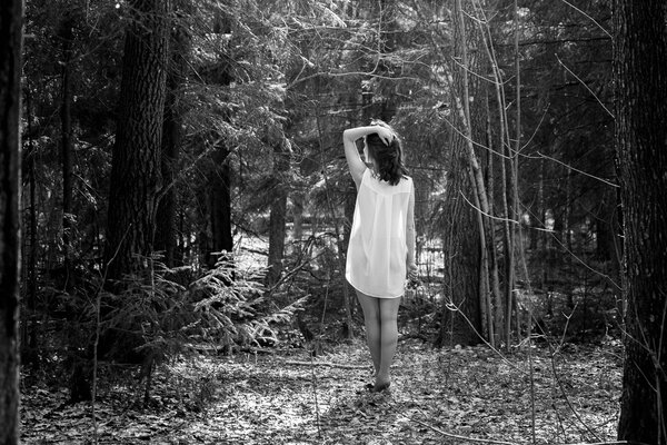 Woman in a white shirt with flowers in her hand goes into the woods
