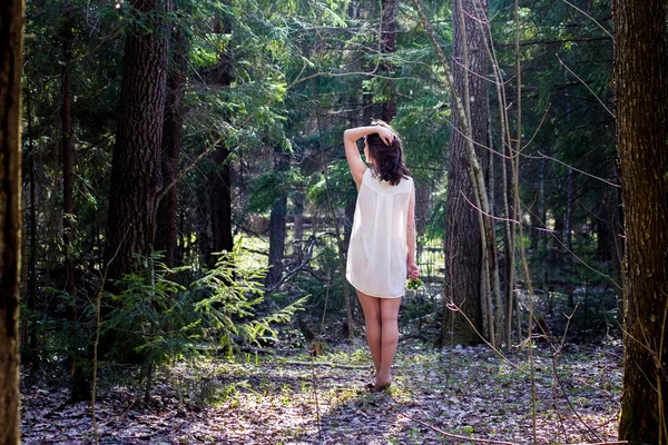 Женщина в белой рубашке с цветами в руке идет в лес — стоковое фото