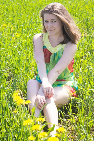 Bella donna con i capelli lunghi seduta su un prato in erba in abito corto verde — Foto Stock