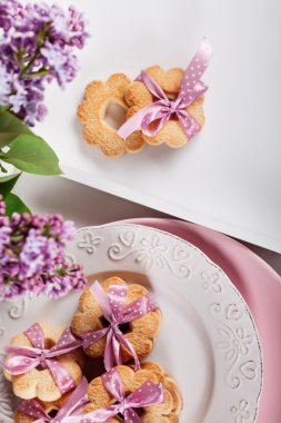 Biscuits with pink ribbon on white plate with lilac flowers