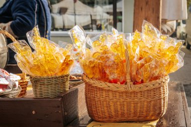 Açık bir ambalajda çubuk üzerinde el yapımı, horoz şeklinde şekerler, açık hava pazarında hasır sepetlerde sergileniyor. Ilık ışıklandırmalar.  