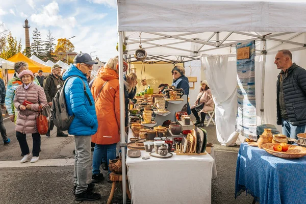 İki kişi sarı bir pazar çadırında el yapımı seramik kaseleri, tabakları ve vazoları toprak tonlarında sergiliyor. Geleneksel çömlek ve halk unsurları görünür. 