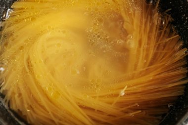 Sıcak suda kızartılmamış bir spagetti görüntüsü, kıvrımlı bir hareket ve görünür kabarcıklar ve köpüklerle altın bir bulanıklık yaratır..