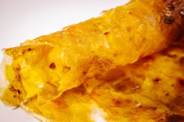 Bir ayva meyvesinin yırtık derisinin yakın çekimi, onun yapış yapış, lifli iç yüzünü ve yumuşak ışıklandırmayla zengin altın turuncu renklerini ortaya koyuyor..