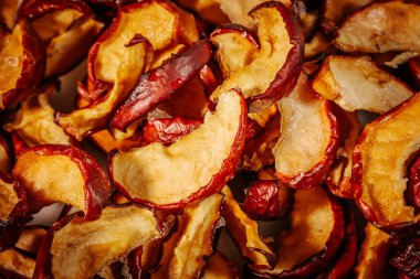 Kurumuş elma dilimlerinin dokusunu ve zengin rengini gösteren ayrıntılı bir makro resim, buruşuk, kırmızı derilerini ve altın tenlerini vurguluyor..