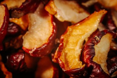 Kurumuş elma dilimlerinin dokusunu ve zengin rengini gösteren ayrıntılı bir makro resim, buruşuk, kırmızı derilerini ve altın tenlerini vurguluyor..