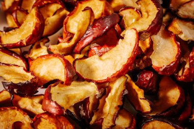 Kurumuş elma dilimlerinin dokusunu ve zengin rengini gösteren ayrıntılı bir makro resim, buruşuk, kırmızı derilerini ve altın tenlerini vurguluyor..