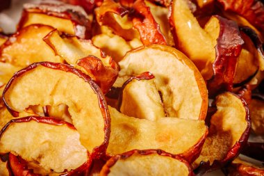 Kurumuş elma dilimlerinin dokusunu ve zengin rengini gösteren ayrıntılı bir makro resim, buruşuk, kırmızı derilerini ve altın tenlerini vurguluyor..