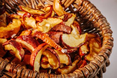 Kurumuş elma dilimleriyle çevrilmiş bir hasır sepet. Kıtır kıtır dokularını ve doğal kırmızı derilerini ortaya çıkarıyor..