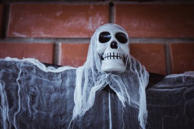 Kırmızı tuğladan bir duvara bağlanmış, kafatası yüzlü, yırtık pırtık bir pelerinli bir ölüm meleğinin yakın çekimi.. 