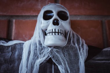 Kırmızı tuğladan bir duvara bağlanmış, kafatası yüzlü, yırtık pırtık bir pelerinli bir ölüm meleğinin yakın çekimi.. 
