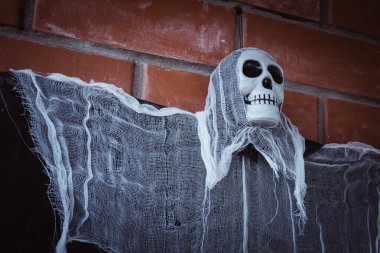 Kırmızı tuğladan bir duvara bağlanmış, kafatası yüzlü, yırtık pırtık bir pelerinli bir ölüm meleğinin yakın çekimi.. 