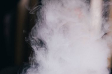 Kısmen örtülü bir adam yoğun duman ya da buharın içinden bakar, sadece bir gözü açıktır, gizemli ve kasvetli bir etki yaratır..