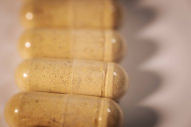 Şeffaf bitkisel takviye kapsüllerinin yakın plan çekimi bir sırada, hafif bir yüzeyde yumuşak zigzag gölgeler oluşturur..