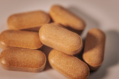 Yumuşak ve hafif bir yüzeye dağılmış oval şekilli kahverengi besin takviyesi hapları. Doğal ışık ve gölgeler dokuyu vurgular.