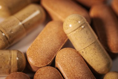 Kapsüller ve tabletler de dahil olmak üzere, nötr bir yüzeyde çeşitli renk ve dokular içeren çeşitli besin takviyelerinin yakın plan görüntüsü.