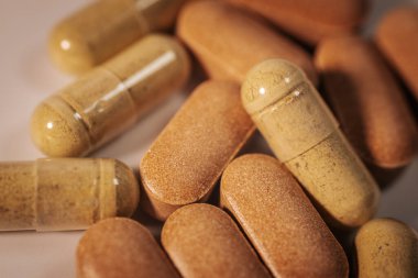 Kapsüller ve tabletler de dahil olmak üzere, nötr bir yüzeyde çeşitli renk ve dokular içeren çeşitli besin takviyelerinin yakın plan görüntüsü.