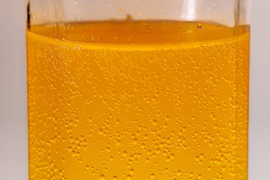 Şeffaf bir bardakta portakal renkli köpüklü bir içecek. Detaylı karbonlaşma kabarcıklarının yükseldiğini gösteriyor. Parlak ve ferahlatıcı görünüş.