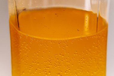 Şeffaf bir bardakta portakal renkli köpüklü bir içecek. Detaylı karbonlaşma kabarcıklarının yükseldiğini gösteriyor. Parlak ve ferahlatıcı görünüş.