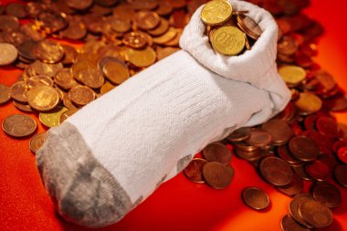 Avro sikkeleri ile doldurulmuş beyaz bir çorap diğer dağınık madeni paraların tepesinde duruyor, bu da gizli tasarrufları veya alışılmadık depolamaları akla getiriyor..